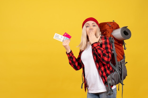 Vista frontal sorprendida chica rubia con su mochila con tarjeta y boleto de viaje