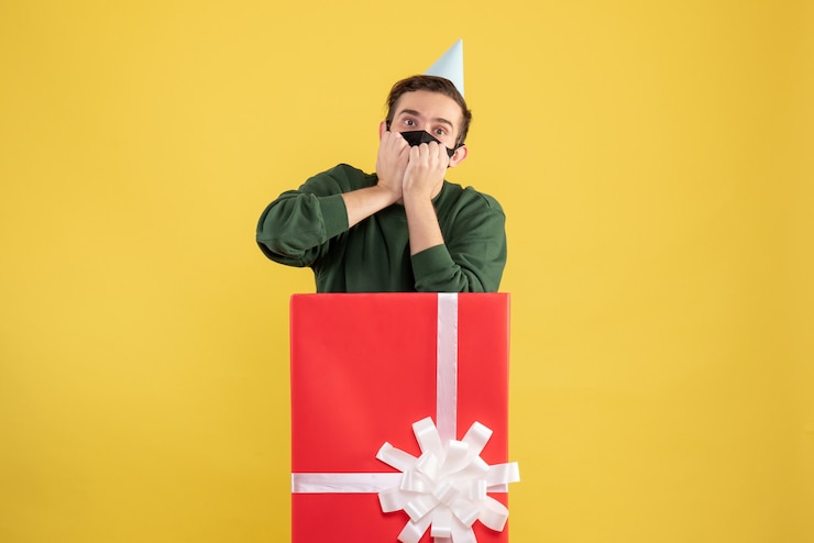 Foto gratuito vista frontal sorprendido joven con gorra de fiesta de pie detrás de caja de regalo grande en amarillo