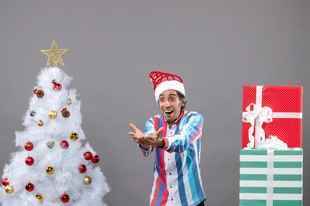 Vista frontal sorprendido joven llamando a alguien cerca del árbol de Navidad blanco