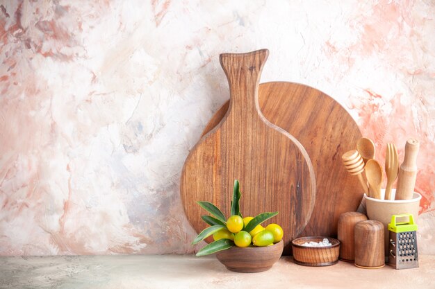 Vista frontal de la tabla de cortar cucharas de madera rallador kumquats en maceta sobre superficie colorida