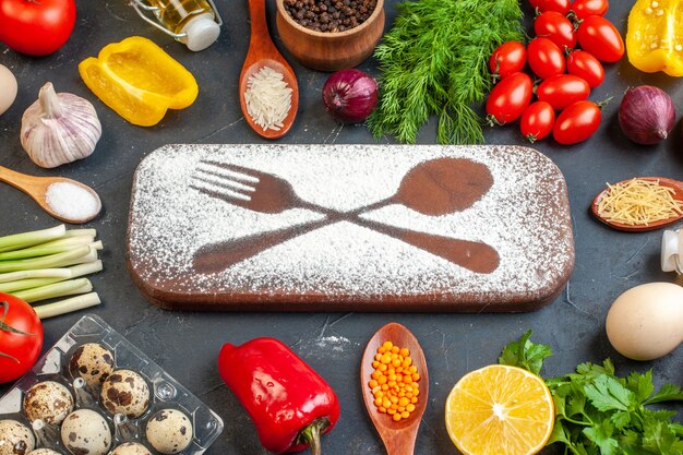 Vista frontal de la tabla de cortar con harina dibujada cuchillo tenedor entre verduras frescas diferentes especias paquetes verdes