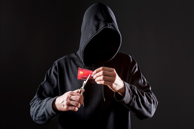 Vista frontal de la tarjeta de crédito de corte de hacker masculino con tijeras