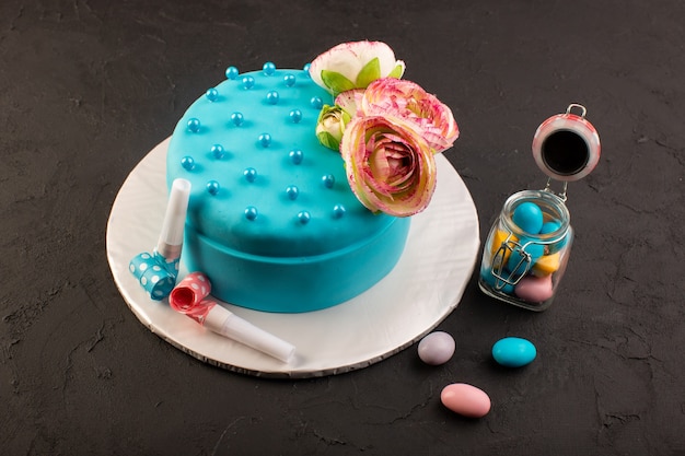 Una vista frontal de la tarta de cumpleaños azul con flores en la parte superior y decoraciones