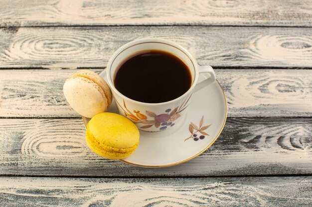 Vista frontal de una taza de café caliente y fuerte con macarons franceses en el escritorio rústico gris café bebida caliente