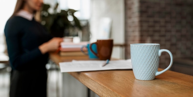 Vista frontal de la taza de café en la mesa con mujer desenfocada