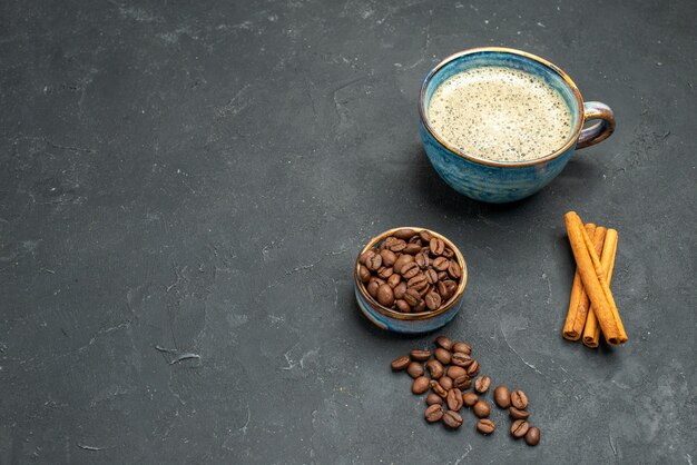 Vista frontal de una taza de café con semillas de café, palitos de canela en la oscuridad con lugar libre