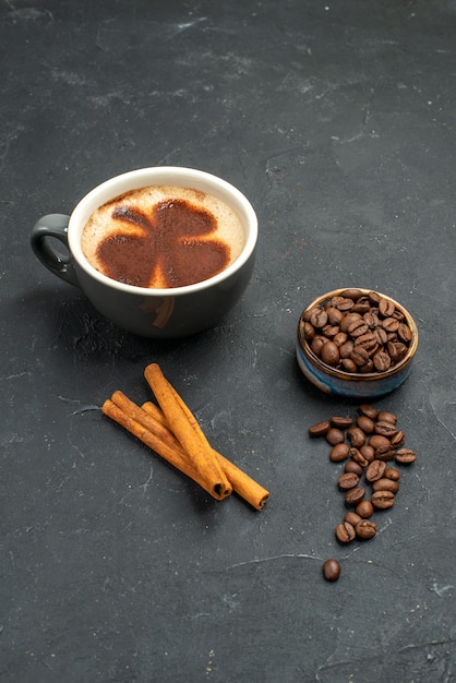 Vista frontal de una taza de café con semillas de granos de café, palitos de canela sobre fondo oscuro aislado lugar libre