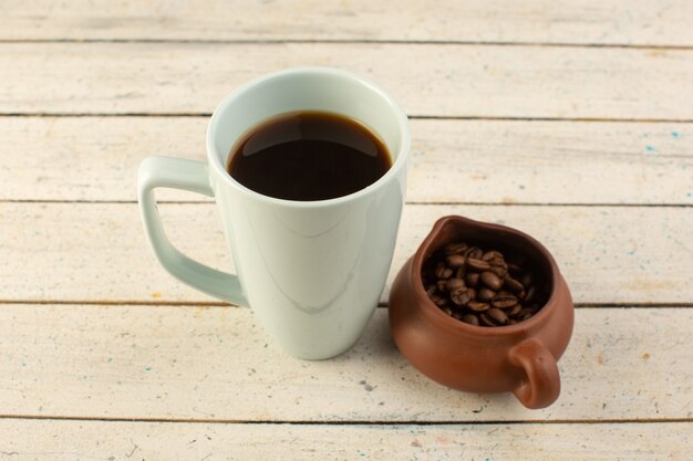 Vista frontal de una taza de café en una taza blanca con semillas de café marrón frescas sobre la superficie clara, beber cafeína