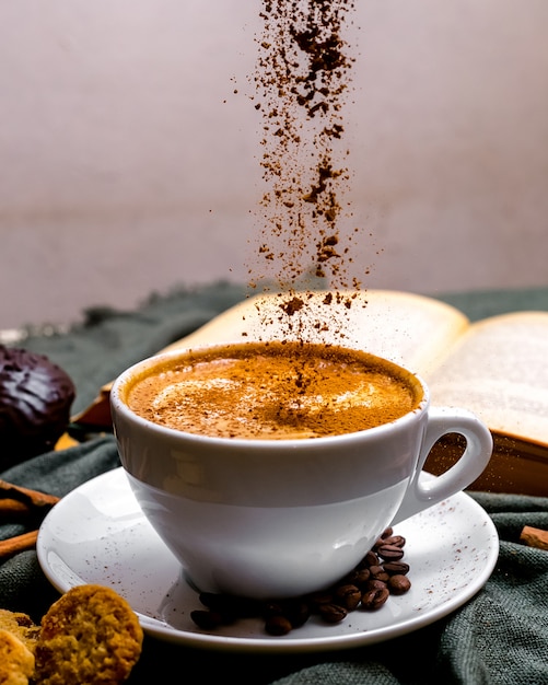 Vista frontal taza de capuchino con galletas y un libro sobre la mesa