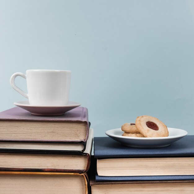 Vista frontal de la taza y la galleta en libros con fondo liso