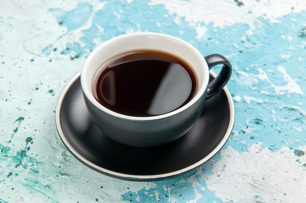 Vista frontal de la taza de té bebida caliente dentro de la taza y el plato en la superficie azul