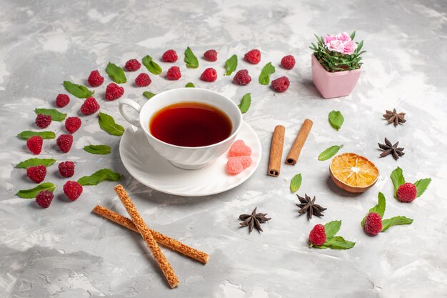 Vista frontal de una taza de té con canela y frambuesas sobre una superficie ligera de té baya canela