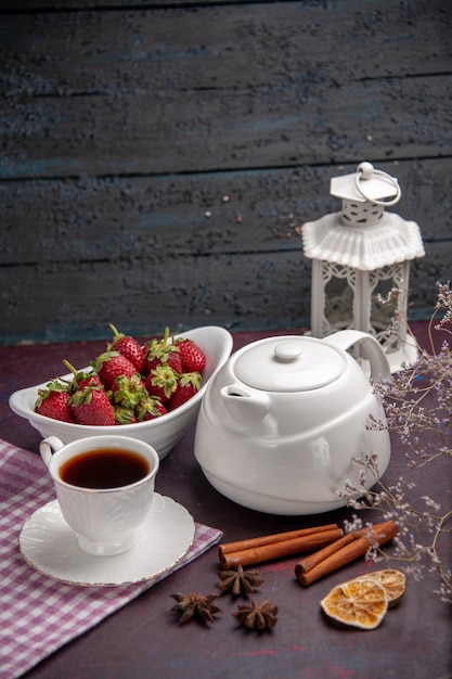 Vista frontal de una taza de té con canela y fresas en la superficie oscura de la bebida de té color de la fruta