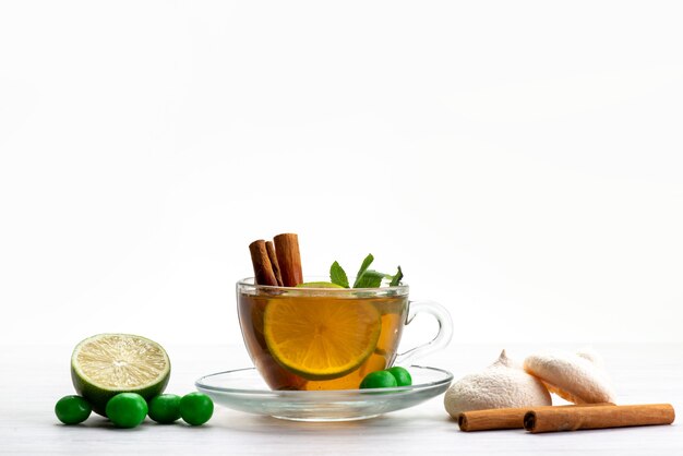 Vista frontal de una taza de té con caramelos de limón y galletas en blanco, dulces de postre de té