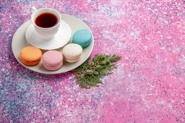 Vista frontal de una taza de té con coloridos macarons franceses en superficie rosa