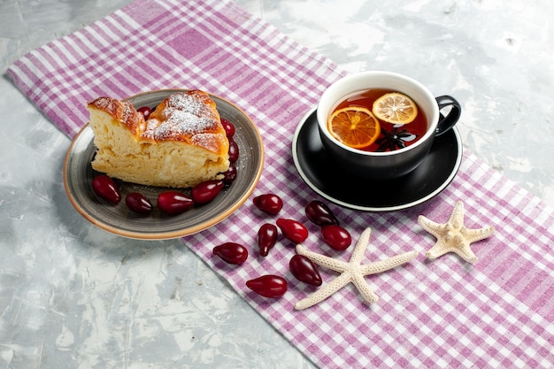 Vista frontal de una taza de té con una deliciosa rebanada de pastel en la superficie blanca