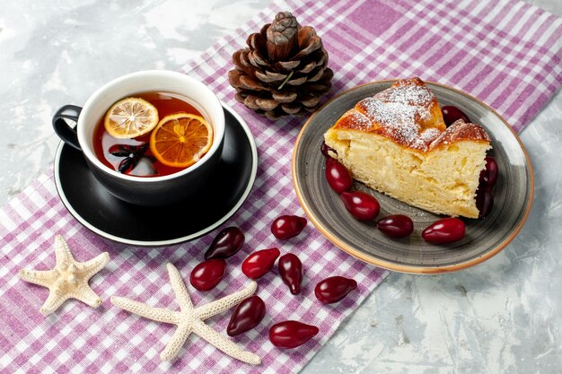 Vista frontal de una taza de té con una deliciosa rebanada de pastel en la superficie blanca