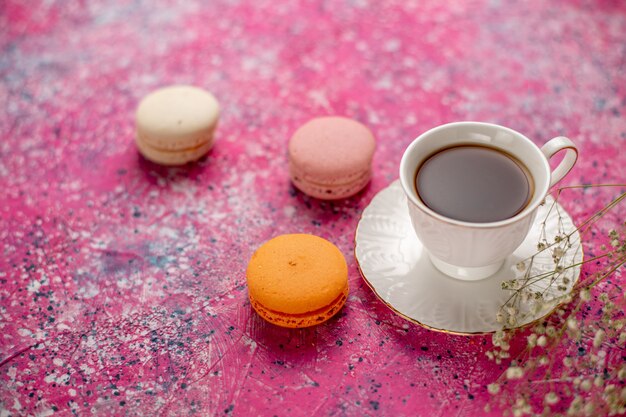 Vista frontal de la taza de té dentro de la taza en un plato con macarons franceses en el escritorio rosa