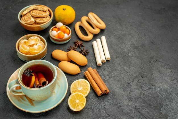 Vista frontal de una taza de té con dulces, galletas y frutas en la mesa gris, té, galleta dulce