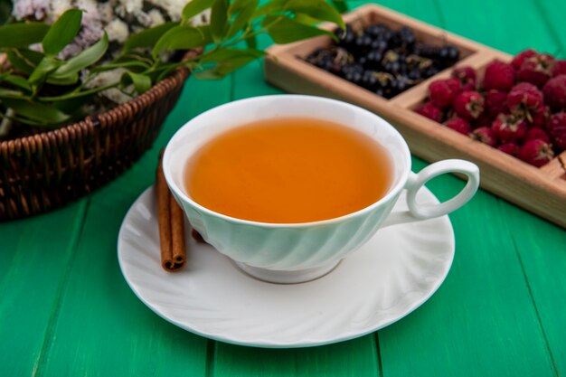 Vista frontal de la taza de té con frambuesas canela y grosellas negras sobre una superficie verde