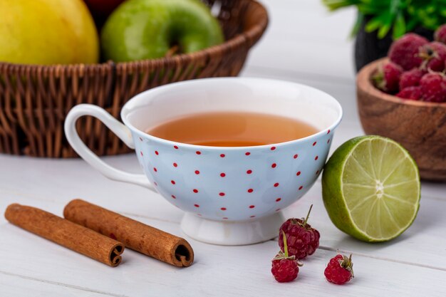 Foto gratuita vista frontal de la taza de té con frambuesas, canela y limón sobre una superficie blanca