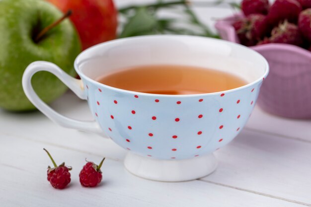 Vista frontal de la taza de té con frambuesas sobre una superficie blanca