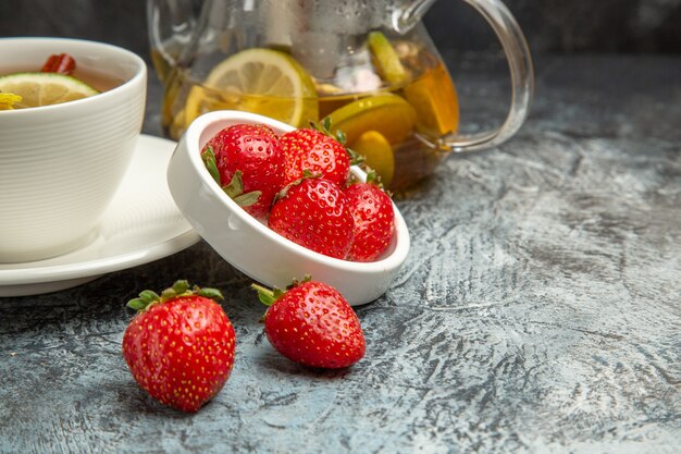 Vista frontal de una taza de té con fresas en la superficie oscura de la baya de té de frutas