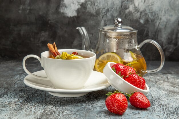 Vista frontal de una taza de té con fresas en la superficie oscura de la baya de té de frutas