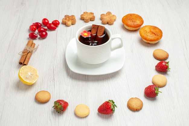 Vista frontal de la taza de té con frutas y galletas en la galleta de postre de té de escritorio blanco