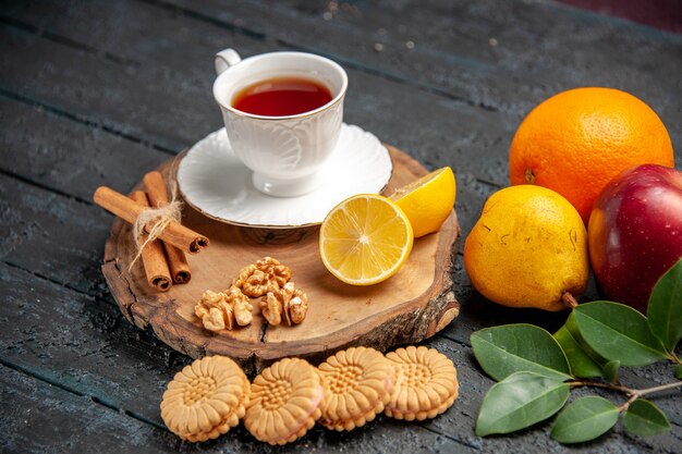 Vista frontal de una taza de té con frutas y galletas en el piso oscuro