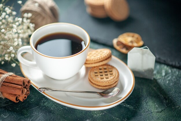 Vista frontal taza de té con galletas dulces en la superficie oscura ceremonia de bebida de pan desayuno foto de la mañana pastel de azúcar colores de vidrio dulce