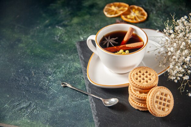 Vista frontal de la taza de té con galletas dulces en la superficie oscura ceremonia de bebida de pan de vidrio dulce desayuno pastel foto en color azúcar