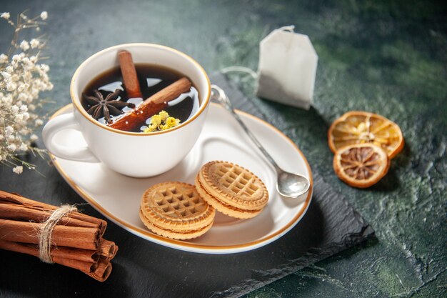 Vista frontal de una taza de té con galletas dulces en la superficie oscura, pan, ceremonia de bebida, desayuno dulce de vidrio, pastel de azúcar de la mañana, fotos en color