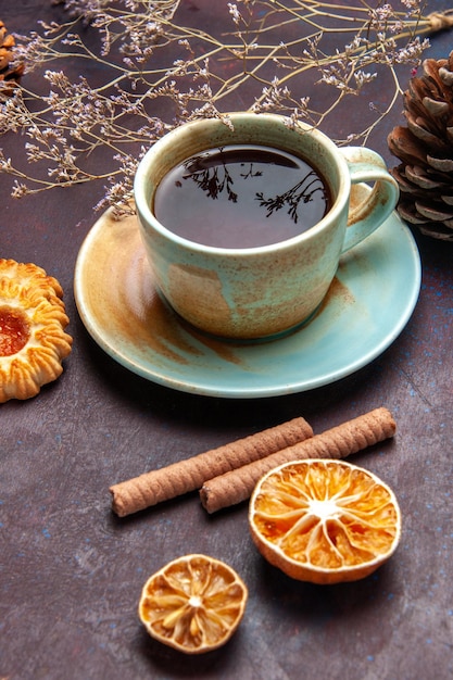 Vista frontal de una taza de té con galletas en un espacio oscuro