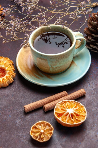 Vista frontal de una taza de té con galletas en un espacio oscuro