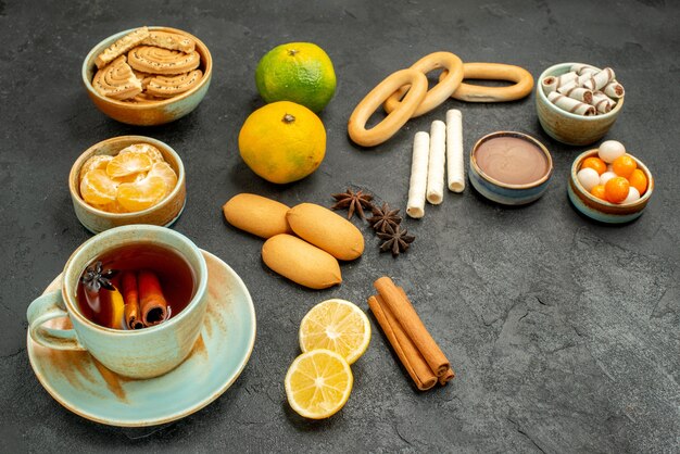 Vista frontal de una taza de té con galletas y frutas en la mesa oscura, pastel, galleta, té, galleta