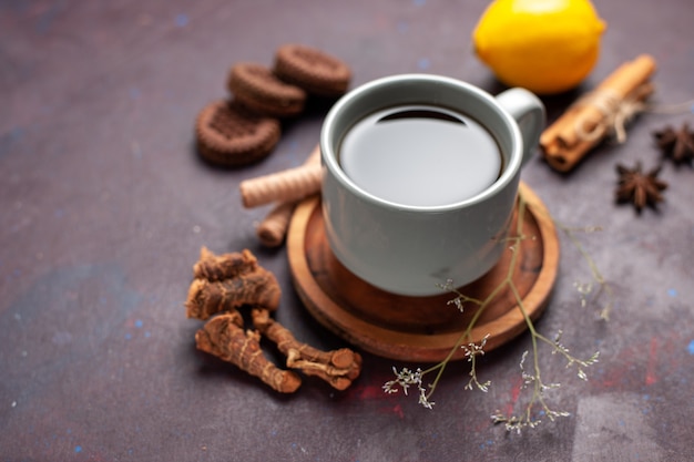 Vista frontal de la taza de té con galletas y limón en la superficie oscura del té color dulce