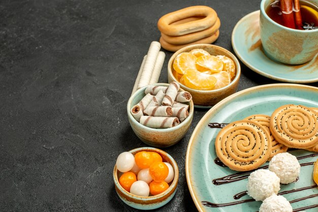 Vista frontal de la taza de té con galletas y mandarinas en el escritorio gris pastel de galletas galletas té