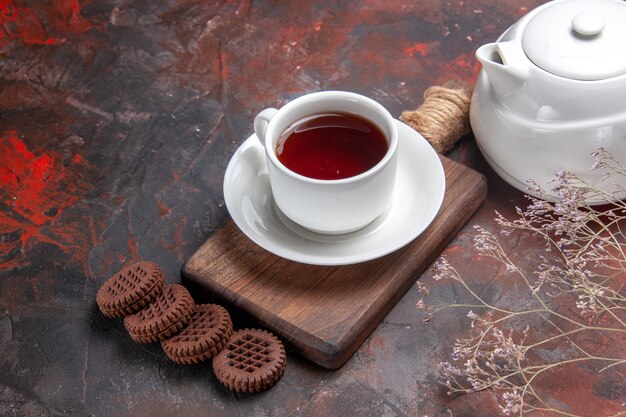 Vista frontal de una taza de té con galletas en la mesa oscura ceremonia de la galleta oscura