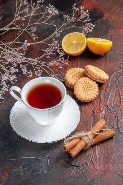 Vista frontal de la taza de té con galletas sobre fondo oscuro