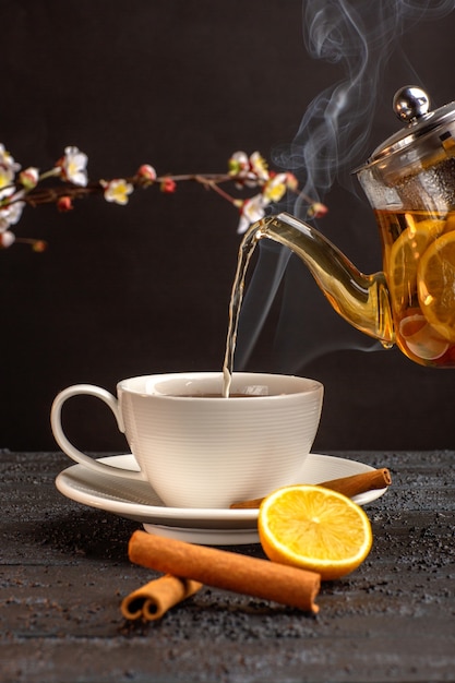 Vista frontal de una taza de té con limón, canela y hervidor de agua en el escritorio gris