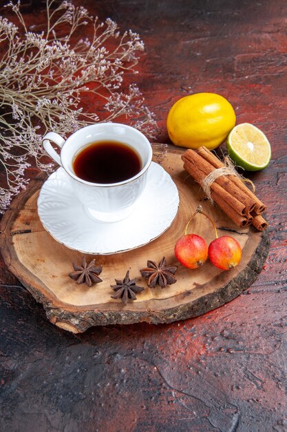 Vista frontal de una taza de té con limón y canela sobre el fondo oscuro