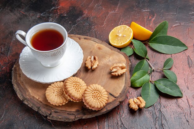 Vista frontal de una taza de té con limón y galletas sobre fondo oscuro