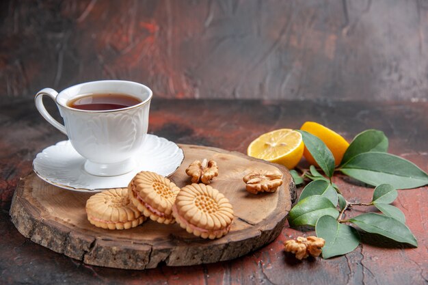 Vista frontal de una taza de té con limón y galletas sobre fondo oscuro