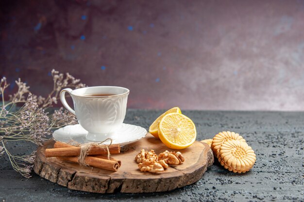 Vista frontal de una taza de té con limón y galletas sobre fondo oscuro