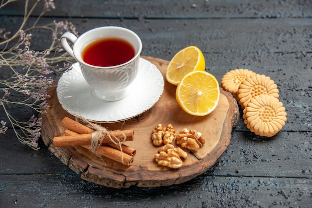 Vista frontal de una taza de té con limón y galletas sobre fondo oscuro