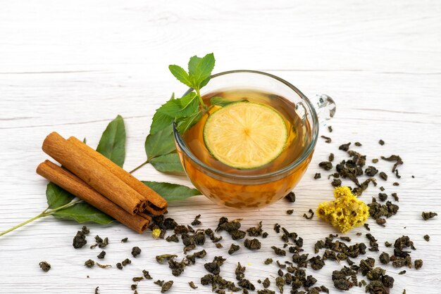 Vista frontal de una taza de té con limón, menta y canela en blanco, dulces de postre de té