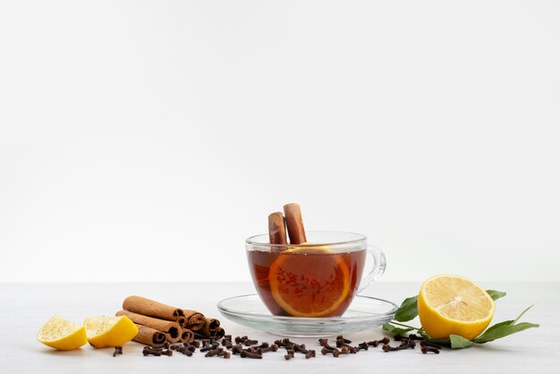 Vista frontal de una taza de té con limón, menta y canela en blanco, dulces de postre de té