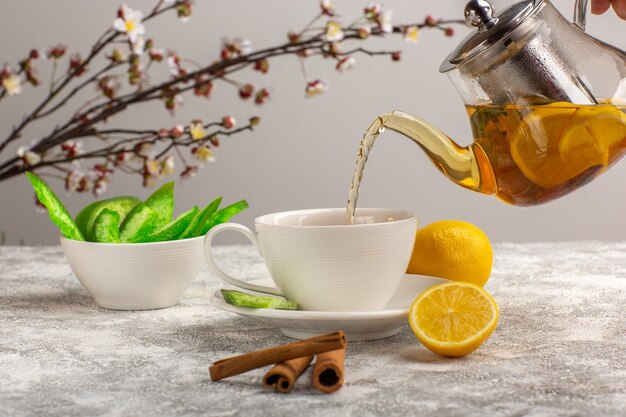 Vista frontal de una taza de té con limones y canela en la superficie de color blanco claro