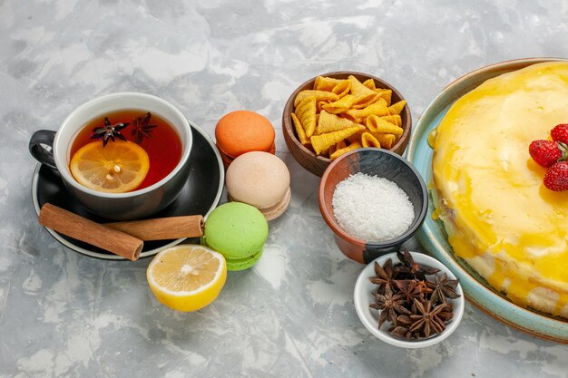 Vista frontal taza de té con macarons franceses y delicioso pastel de sirope amarillo sobre superficie blanca